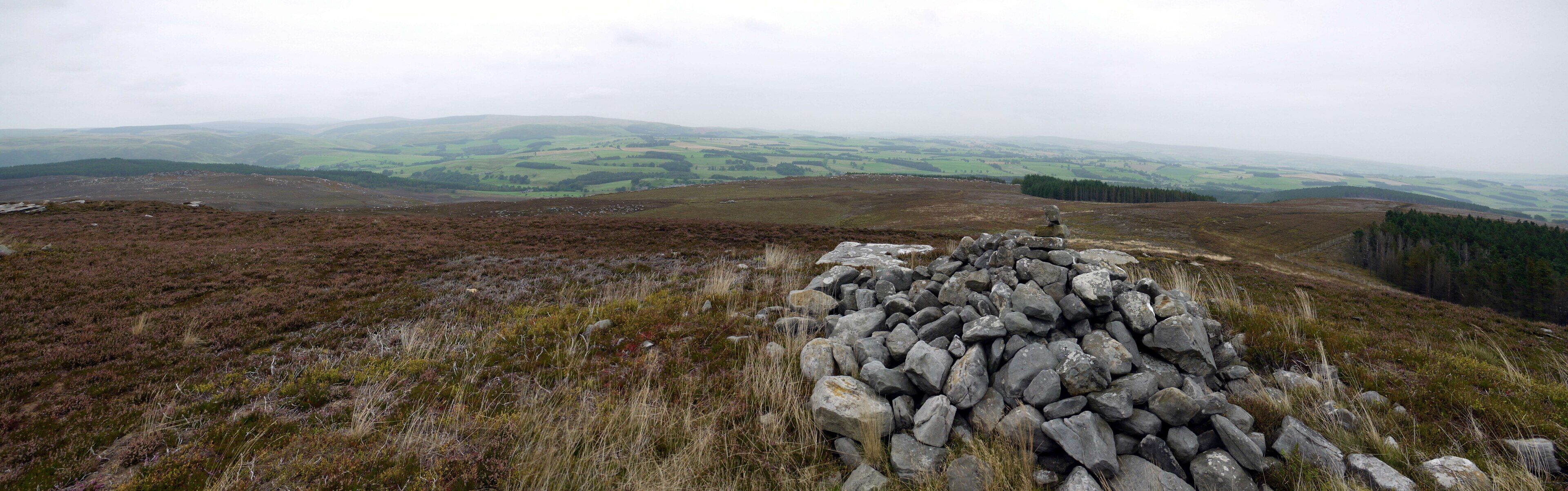 A rocky outcrop with a view of rolling hills and distant trees.