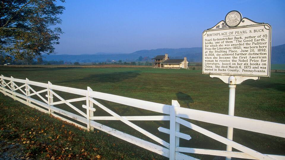 A white fence, a sign, and a building in a rural landscape.