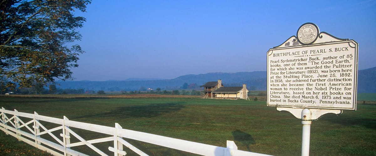 A white fence, a sign, and a building in a rural landscape.