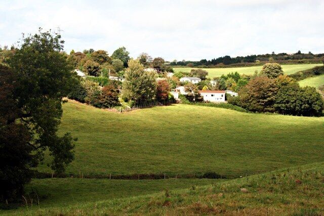 A rural landscape with rolling hills, a white house, and scattered trees.