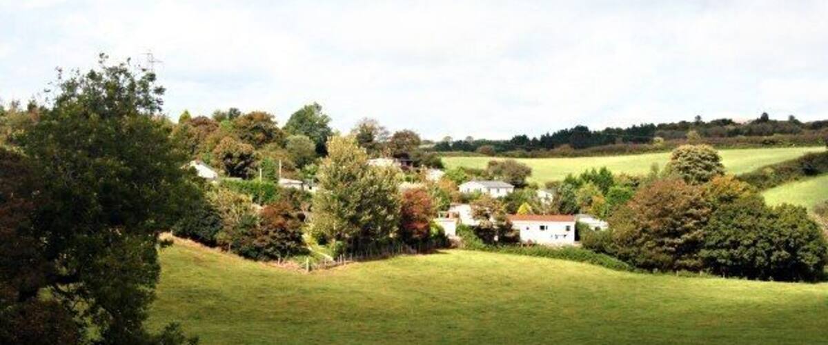 A rural landscape with rolling hills, a white house, and scattered trees.
