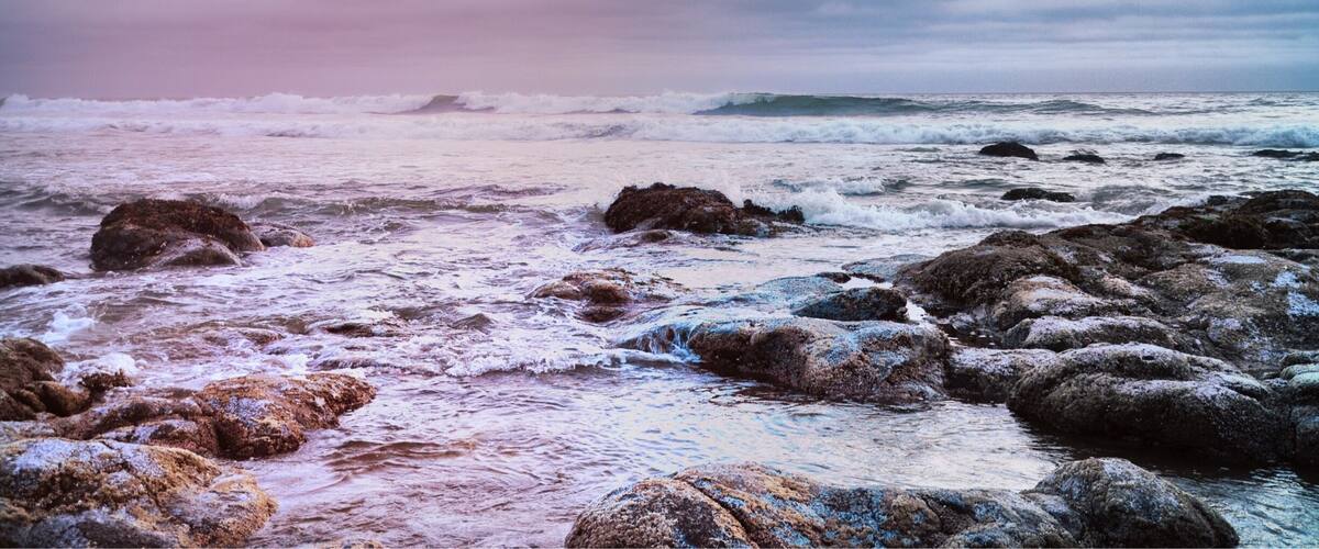 A rocky shoreline with waves crashing against the rocks under a cloudy sky.