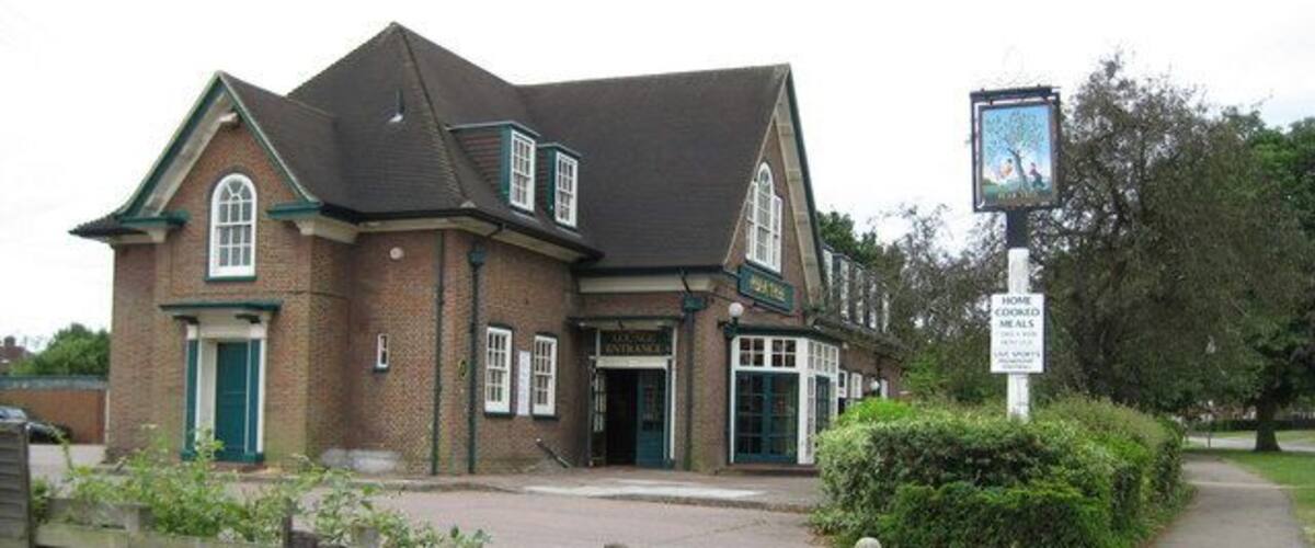 A traditional brick building with a green door and windows, a signboard, and a paved entrance area.