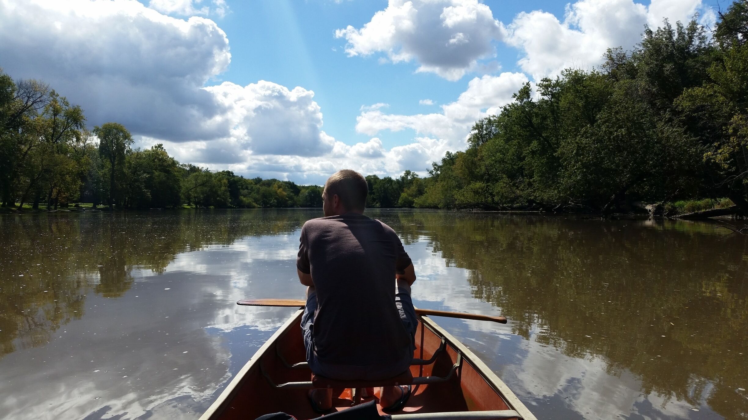 A man paddling a canoe on a calm river surrounded by dense trees.
