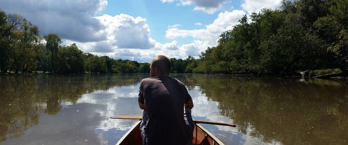 A man paddling a canoe on a calm river surrounded by dense trees.
