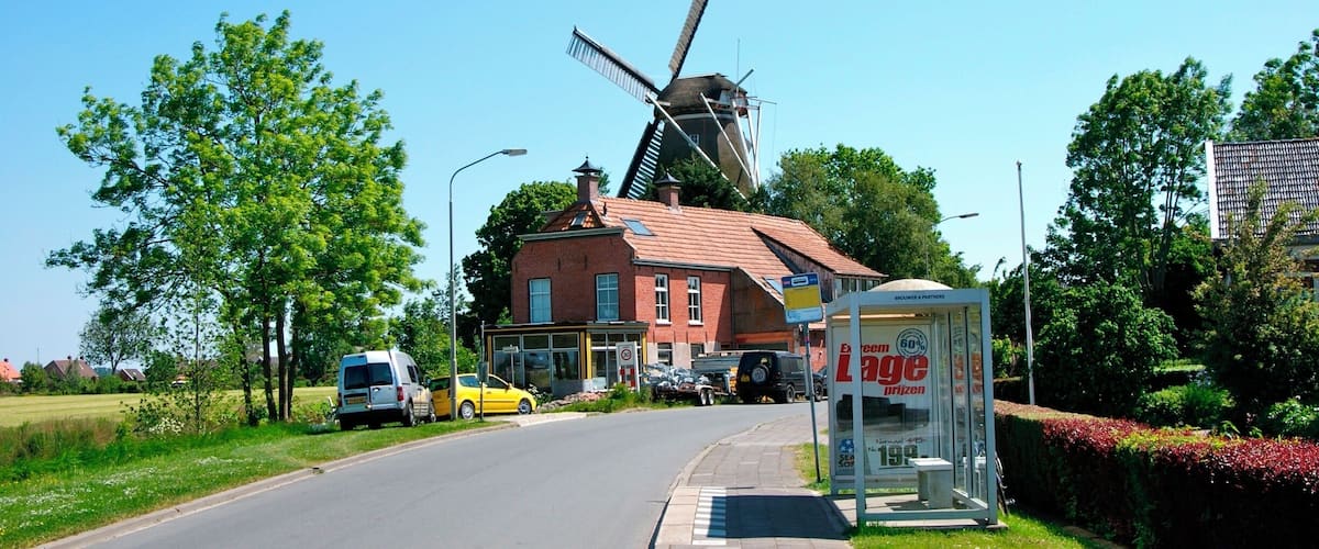 A rural road with a windmill, a red brick building, and a bus stop.