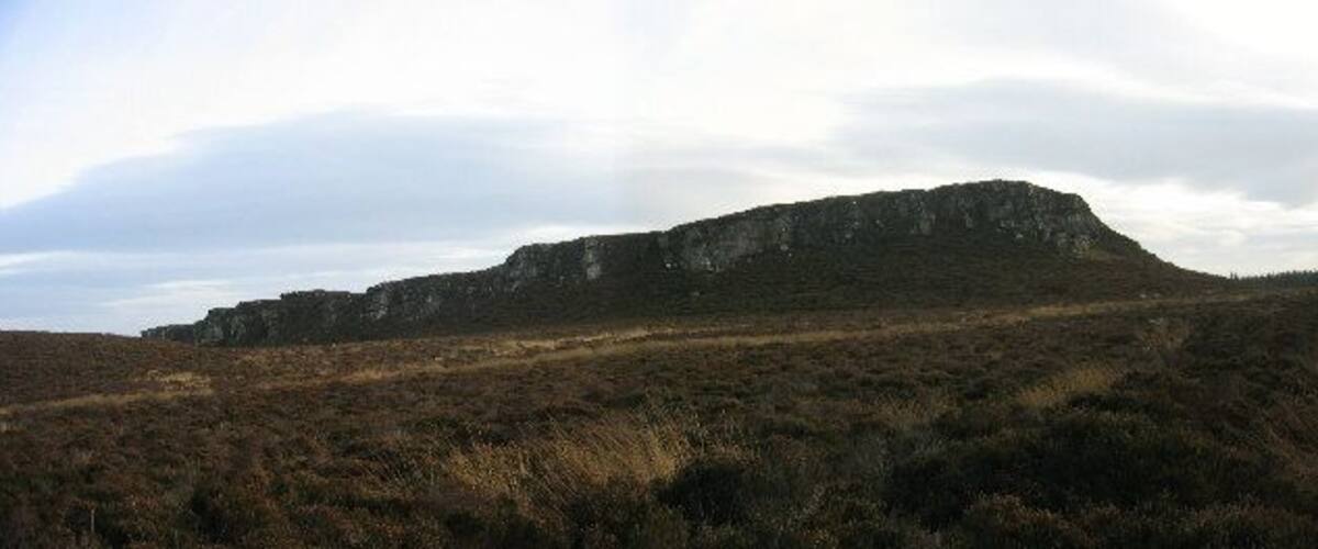 A barren hill with sparse vegetation and a cloudy sky.