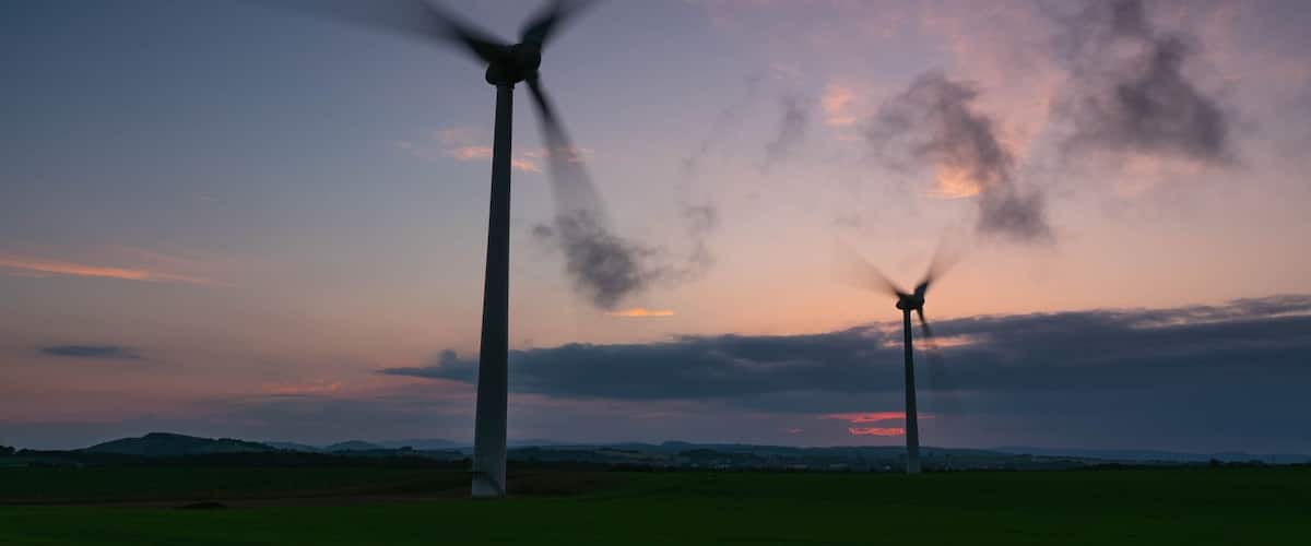 Two wind turbines silhouetted against a sunset sky.
