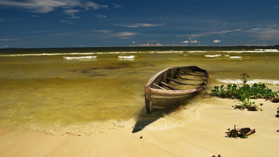 A boat on a sandy beach with clear water and a blue sky.