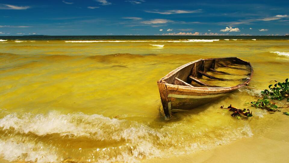 A wooden boat stranded on a beach with clear water and a blue sky.