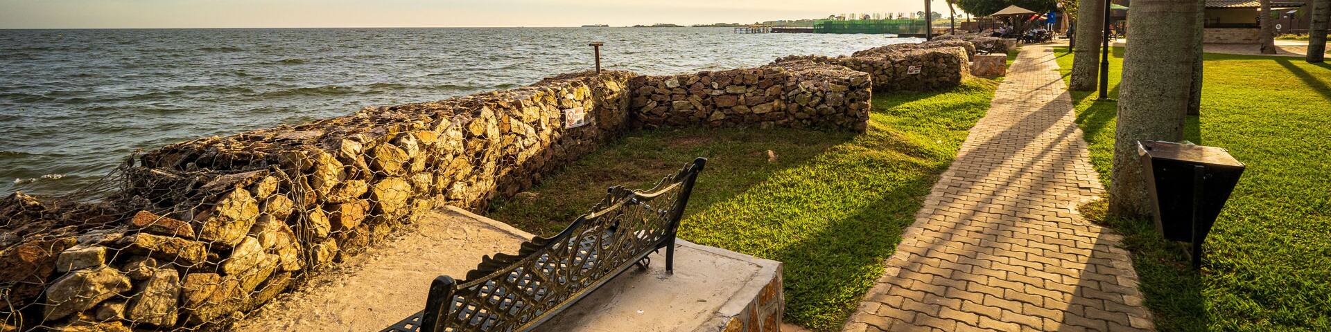 View of the walkway and a wrought iron park bench on the shore of Lake Victoria in Entebbe, Uganda, during the last rays of sunlight in the evening