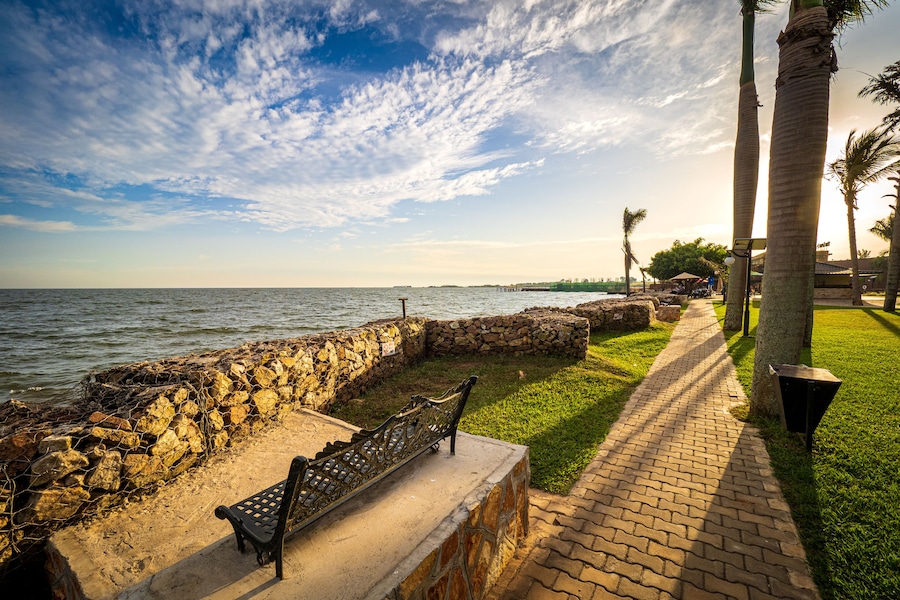 View of the walkway and a wrought iron park bench on the shore of Lake Victoria in Entebbe, Uganda, during the last rays of sunlight in the evening