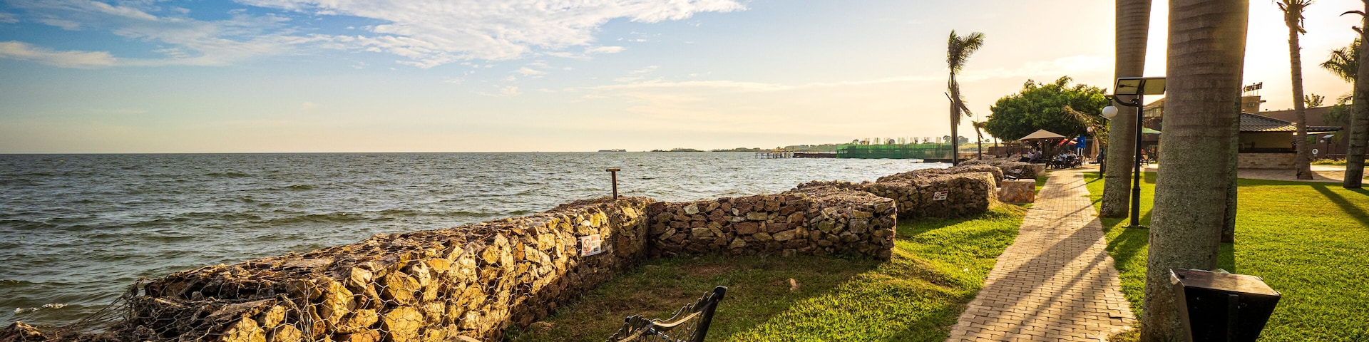 View of the walkway and a wrought iron park bench on the shore of Lake Victoria in Entebbe, Uganda, during the last rays of sunlight in the evening