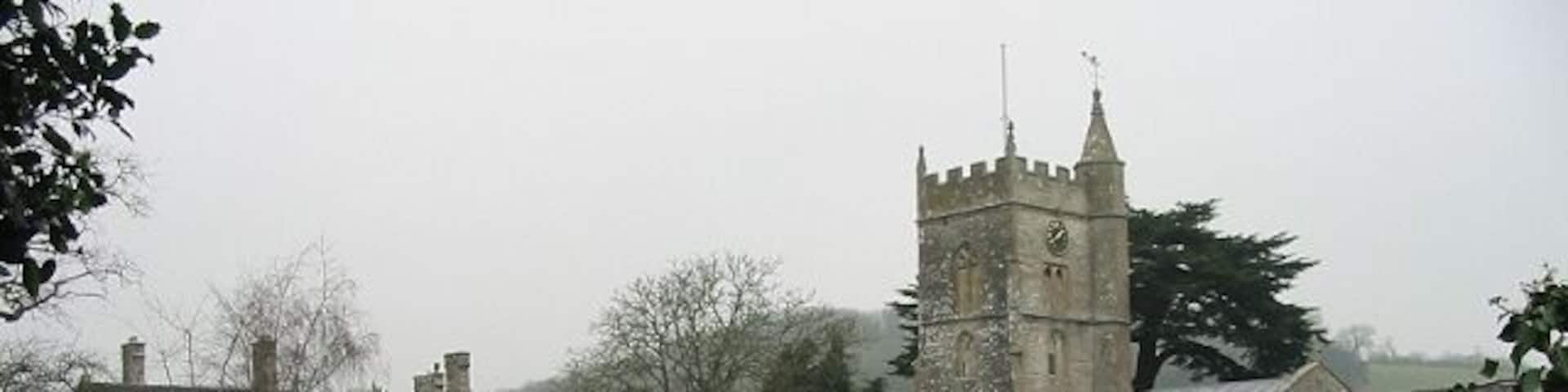 A rural path leading to a church with a tower, surrounded by green fields and a stone building.