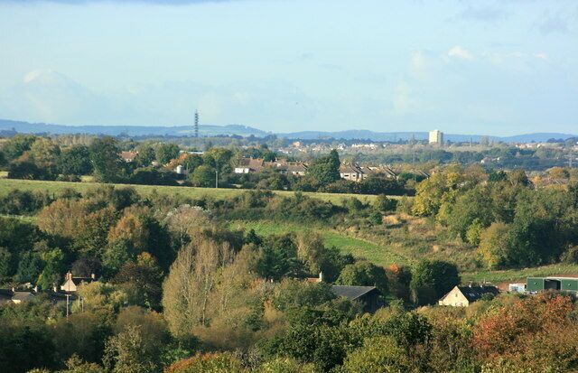 A rural landscape with rolling hills, scattered houses, and a distant tower.