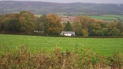 Hartrow Manor. Lying in the valley between the Quantocks and the Brendon Hills, the house is well sheltered by mature trees. The photograph is taken from the B3224 looking north east with the Quantocks in the background.