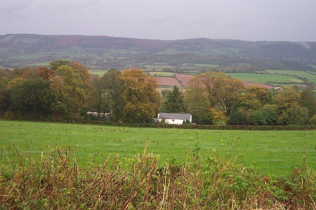 A rural landscape with a white house, rolling hills, and autumn-colored trees.