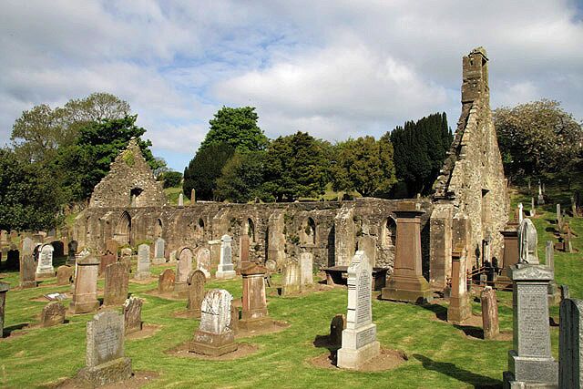 An ancient stone church ruin with multiple tombstones and a grassy cemetery.