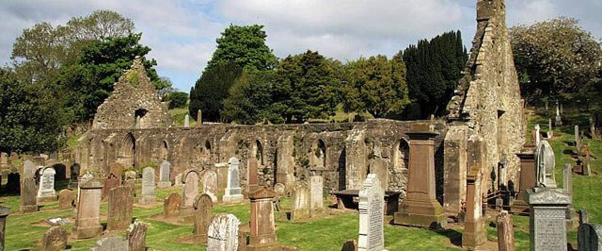 An ancient stone church ruin with multiple tombstones and a grassy cemetery.