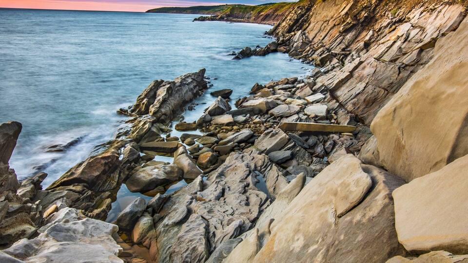 A rocky coastline with large boulders and waves crashing against the shore.