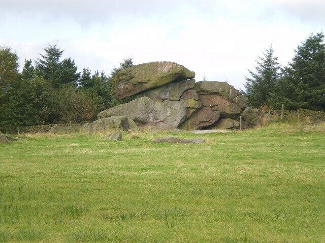 Una gran formación rocosa en un campo cubierto de hierba, con árboles al fondo.