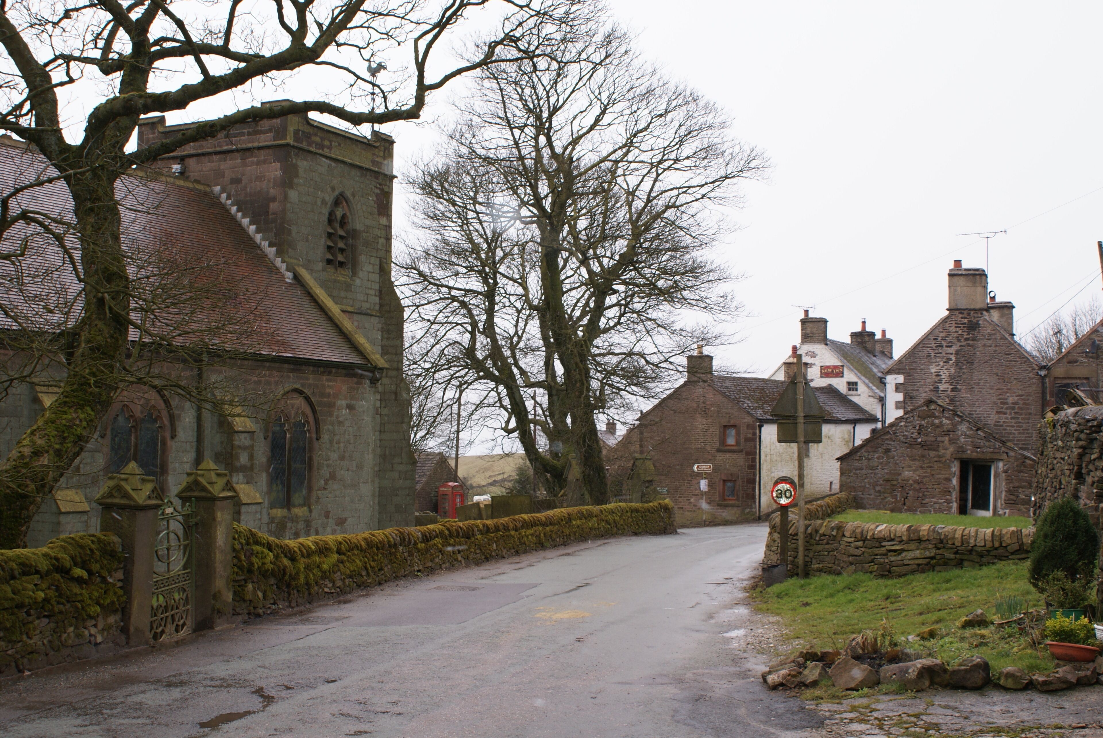 A narrow village road flanked by stone buildings and a church with a moss-covered gate.