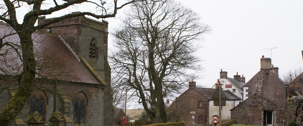 A narrow village road flanked by stone buildings and a church with a moss-covered gate.