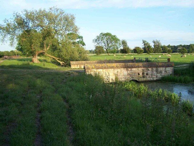 A stone bridge over a river, surrounded by grassy fields and trees.