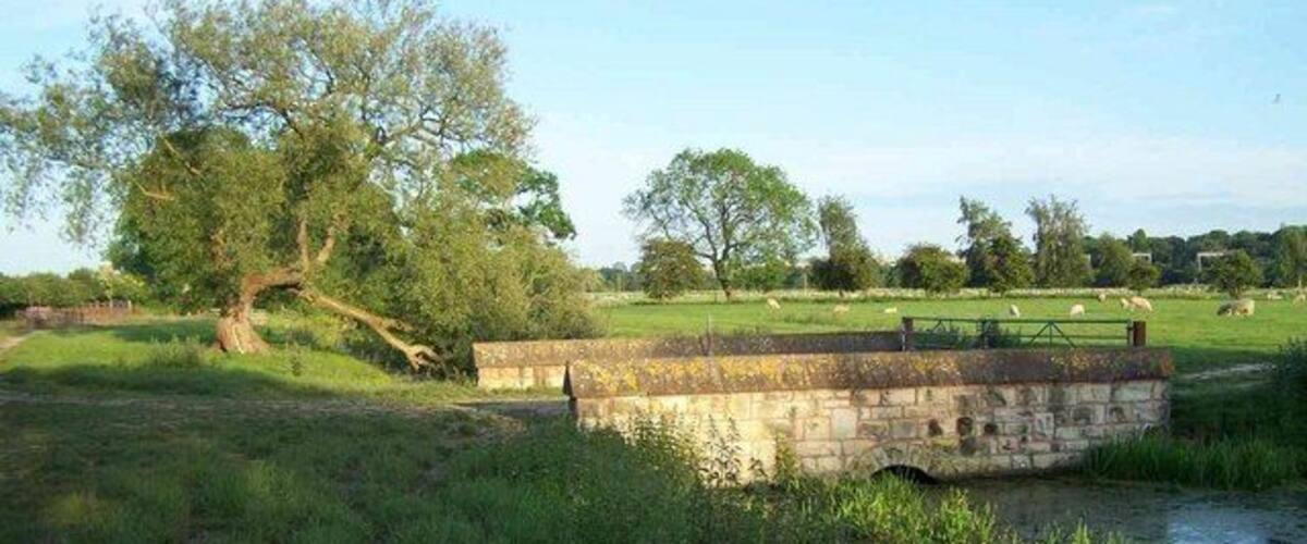 A stone bridge over a river, surrounded by grassy fields and trees.