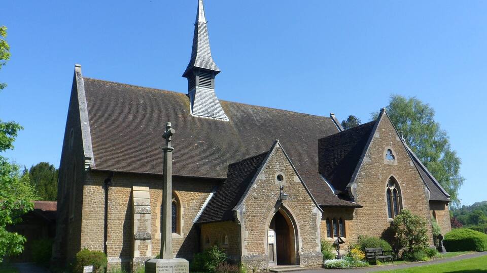 A church with a tall steeple, stone walls, and a well-maintained lawn.
