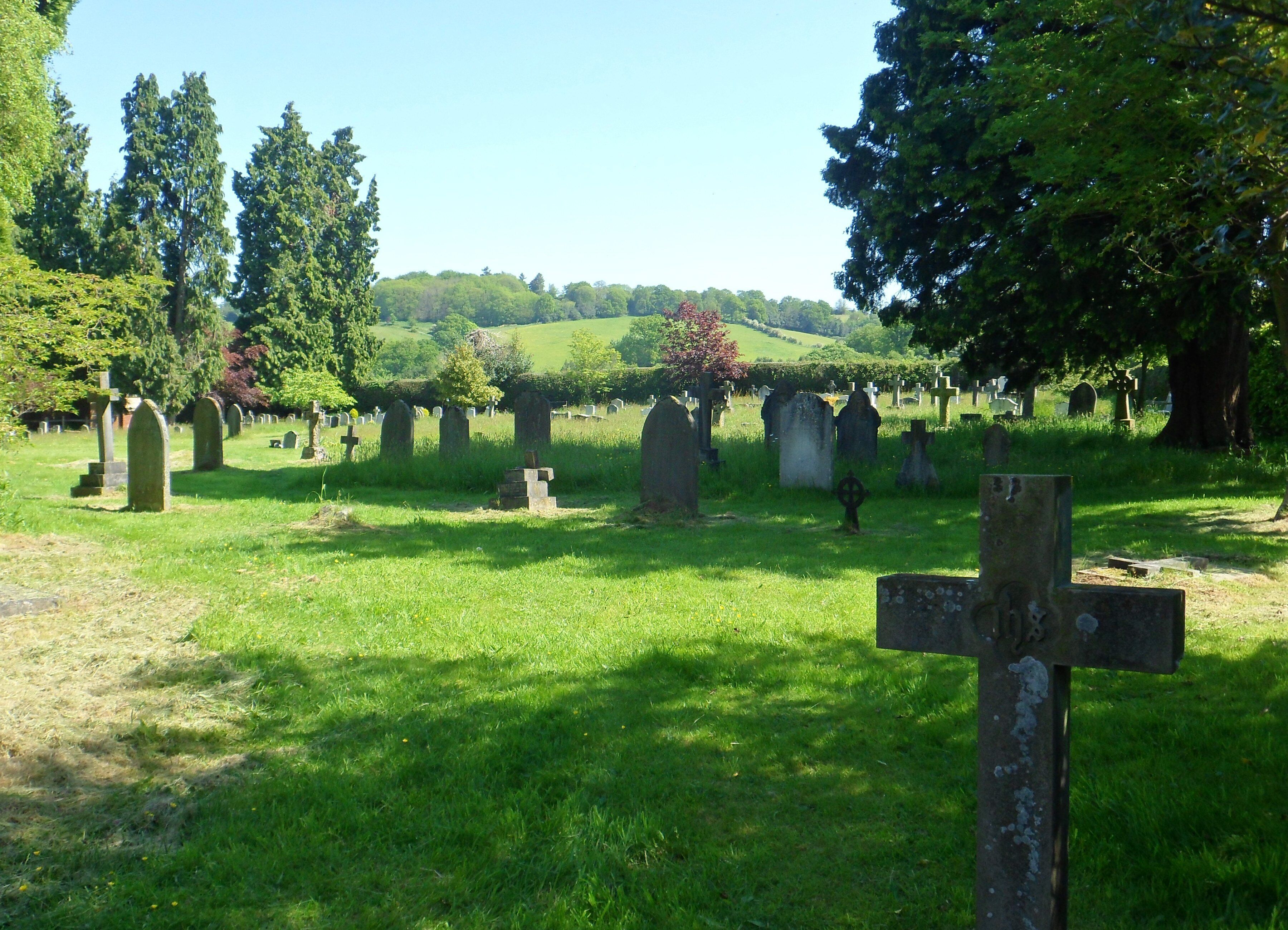 A cemetery with numerous headstones and crosses, surrounded by lush green grass and trees.