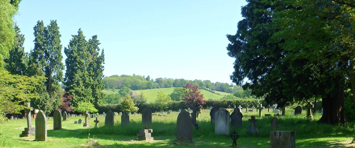 A cemetery with numerous headstones and crosses, surrounded by lush green grass and trees.