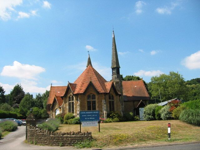 A church with a tall spire, surrounded by greenery and a clear sky.