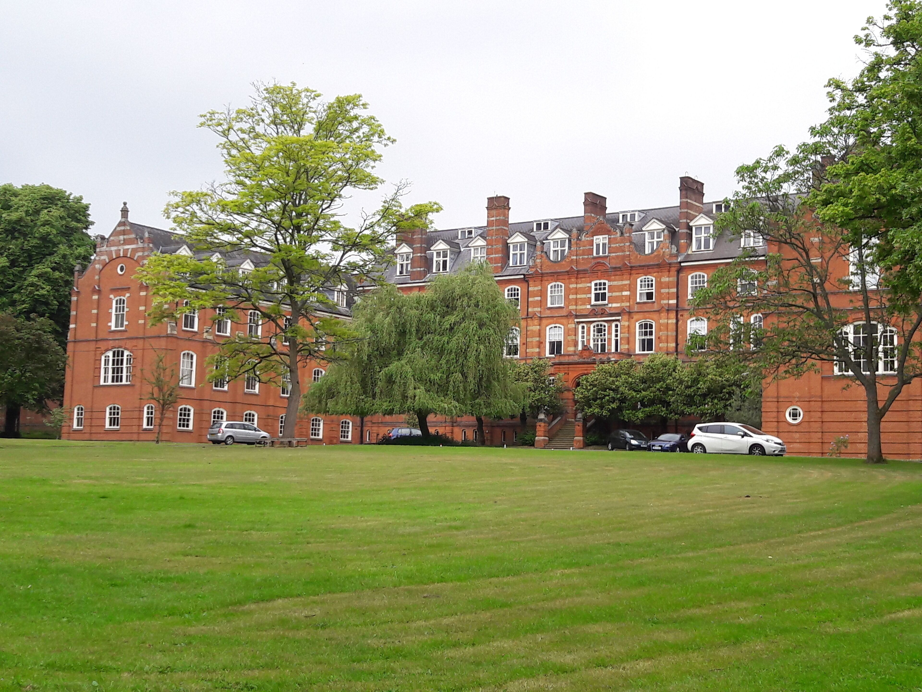 A large red brick building with multiple windows and a lawn in front.