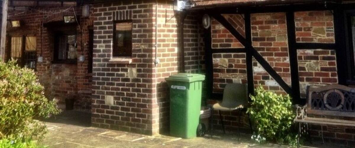 A traditional brick house with a steeply pitched roof and a small attached structure with a chimney.