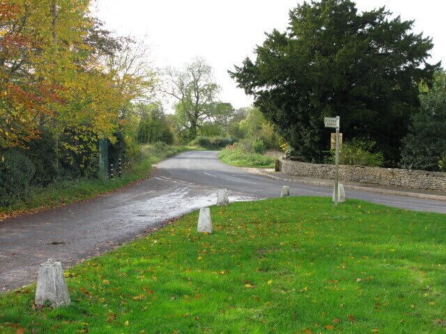 A rural road with a stone wall on one side and a grassy area with trees on the other.