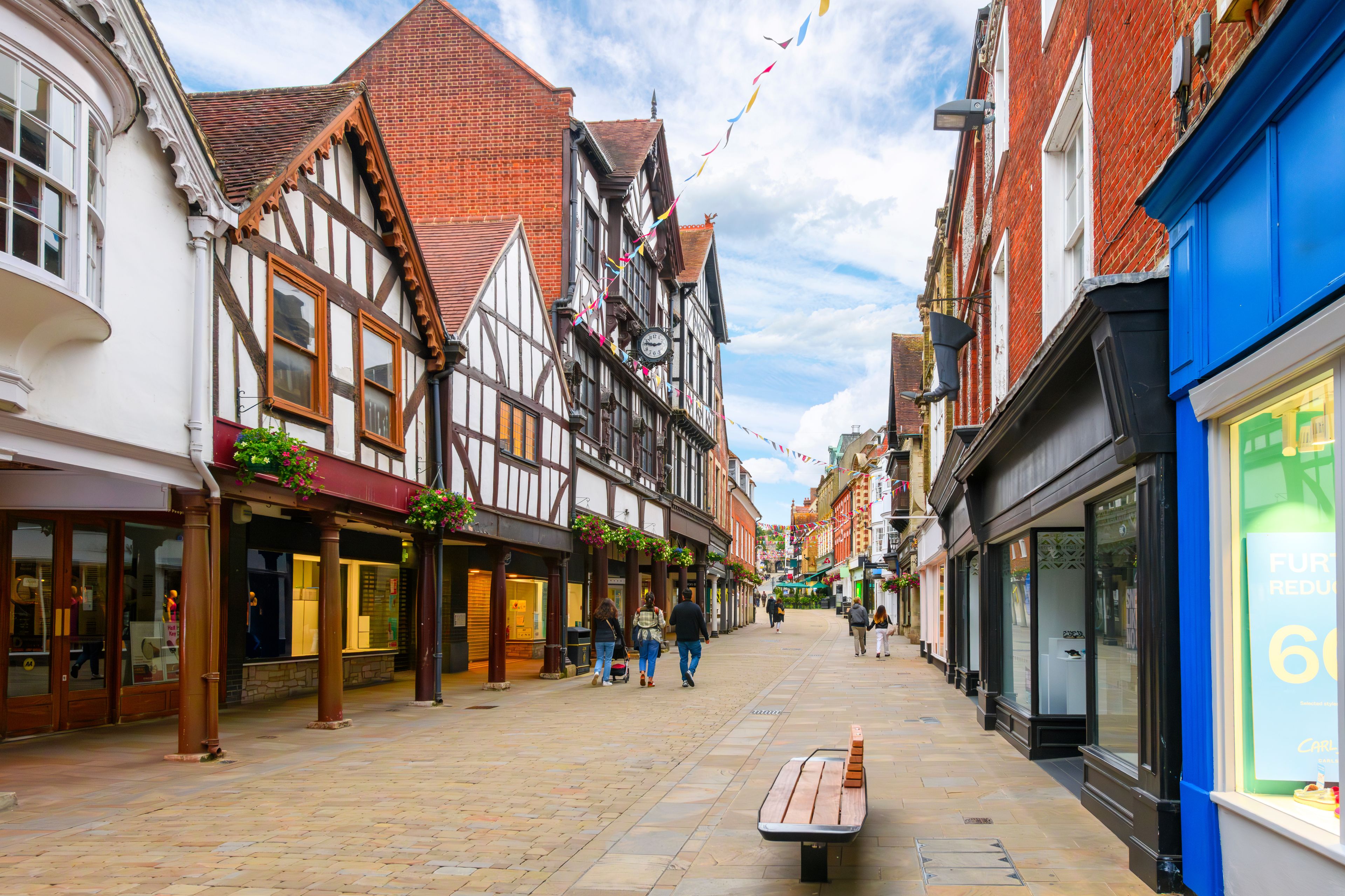 A cobblestone street lined with traditional half-timbered buildings, a bench, and a clear blue sky.