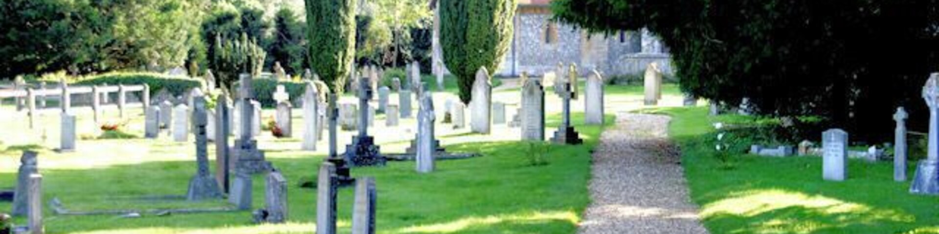 Un cementerio con lápidas, un camino de grava y árboles.