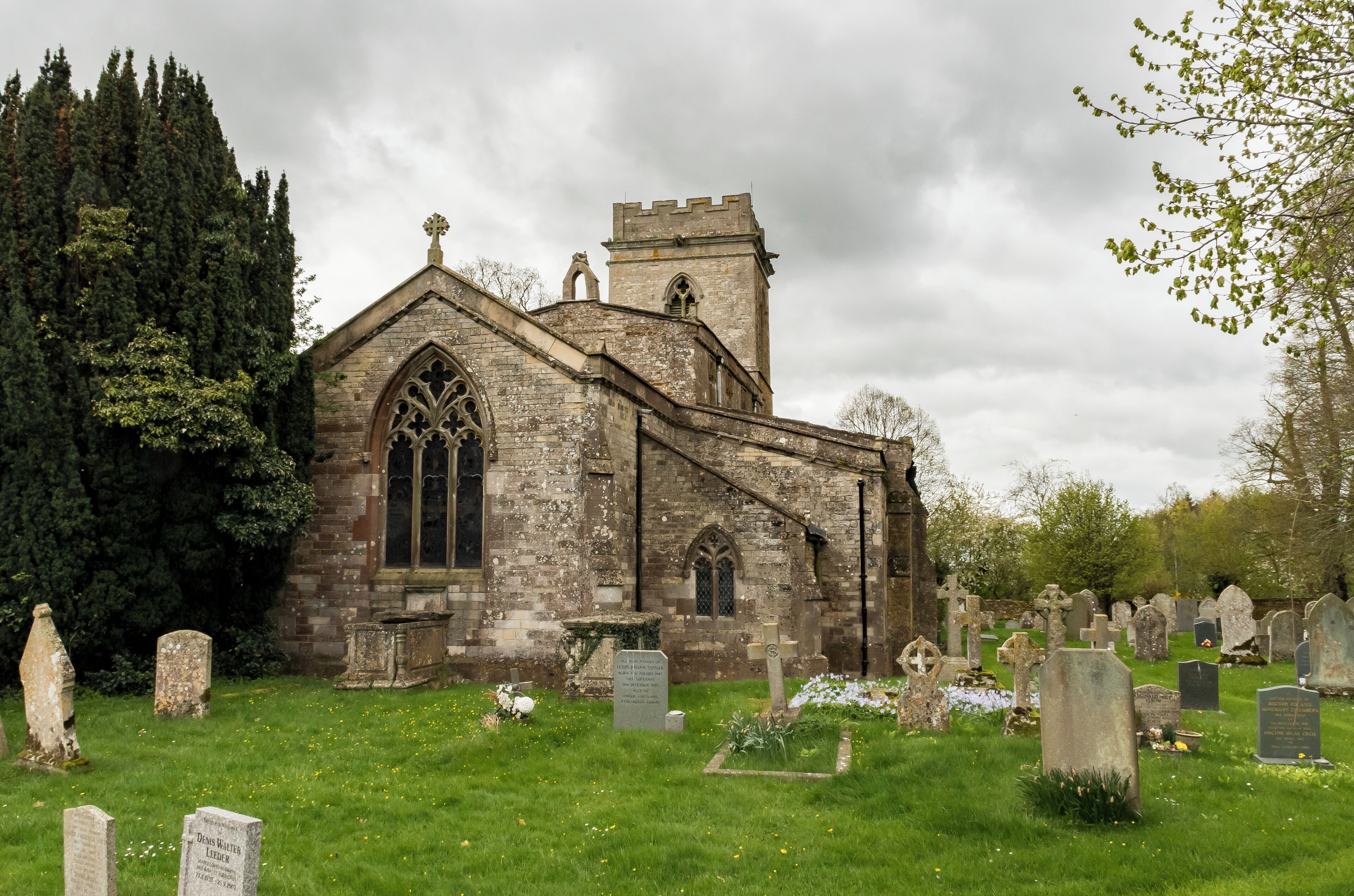 A historic church with a tower and Gothic windows, surrounded by a cemetery with various headstones.