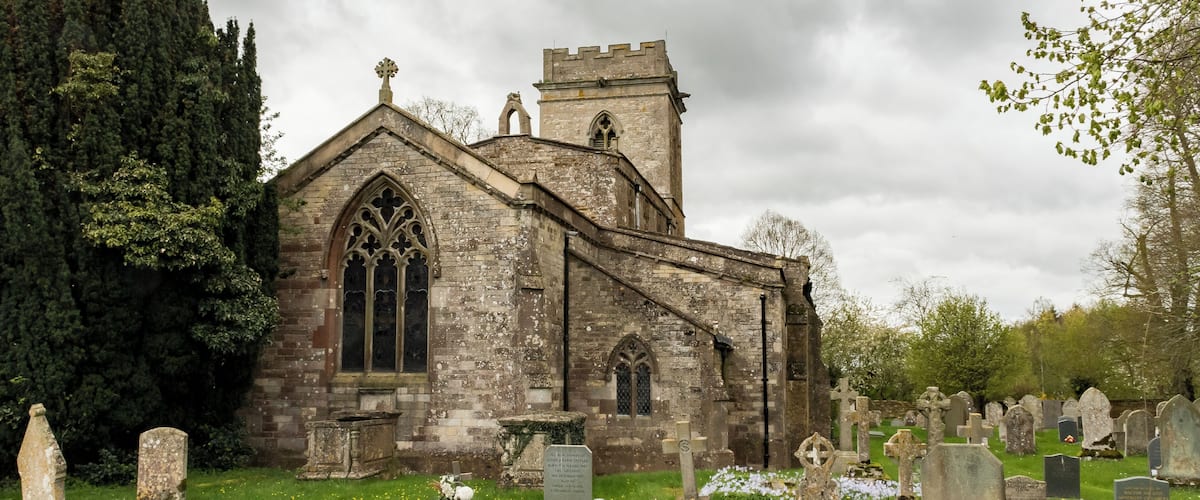 A historic church with a tower and Gothic windows, surrounded by a cemetery with various headstones.