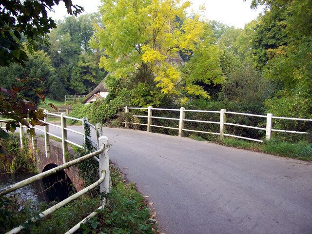 Uma estrada estreita com cerca branca e uma pequena ponte sobre um riacho.