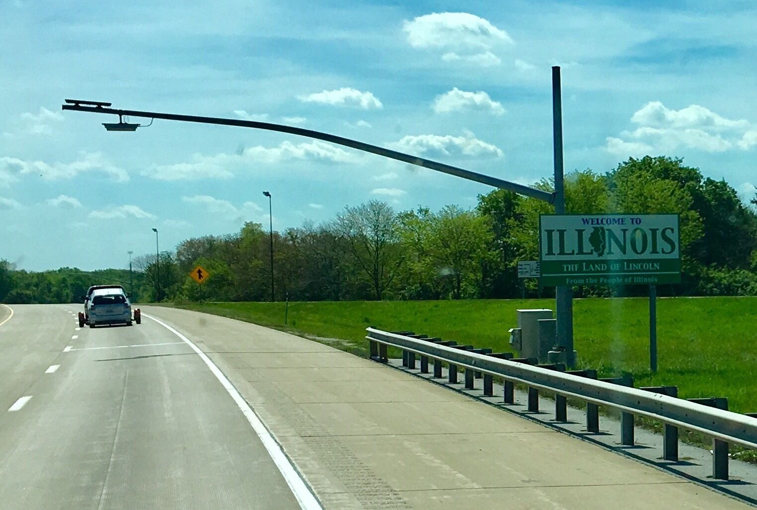 A highway with a 'Welcome to Illinois' sign, a car, and a guardrail.