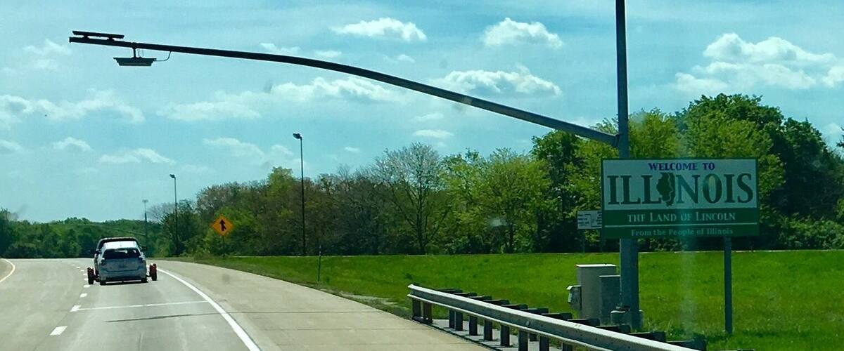 A highway with a 'Welcome to Illinois' sign, a car, and a guardrail.