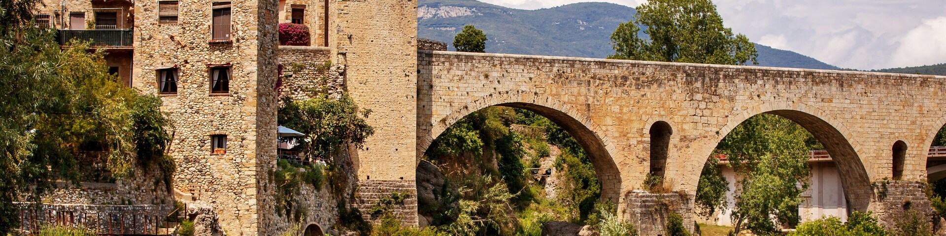 Young mother with her teenager son walking near old bridge over the river Fluvia in unique medieval town of Besalu, province Girona, Spain