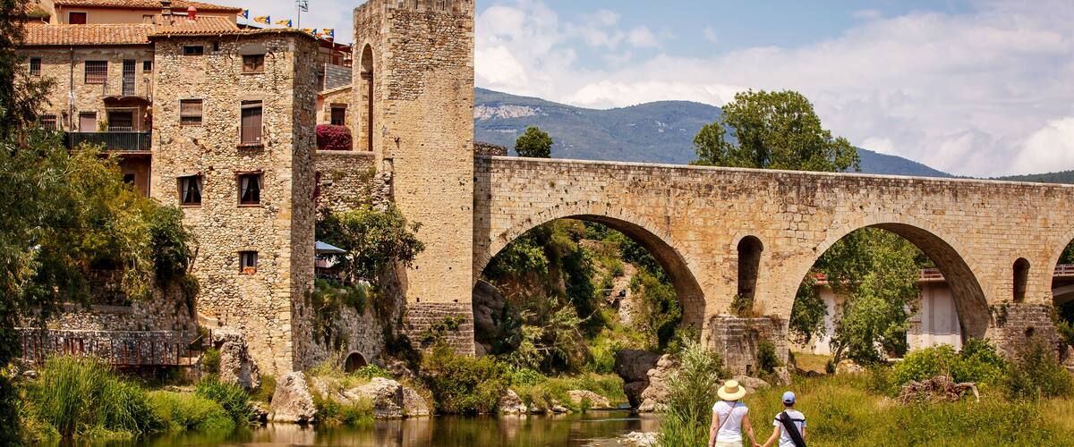 A stone bridge over a river, surrounded by greenery and historic buildings.