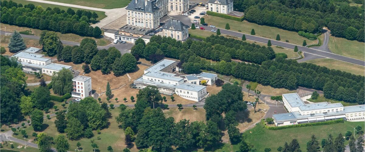An aerial view of a large estate with multiple buildings, surrounded by dense forests and a winding road.