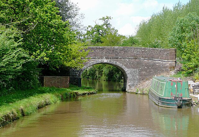 A stone bridge over a river, a green boat, and lush greenery.