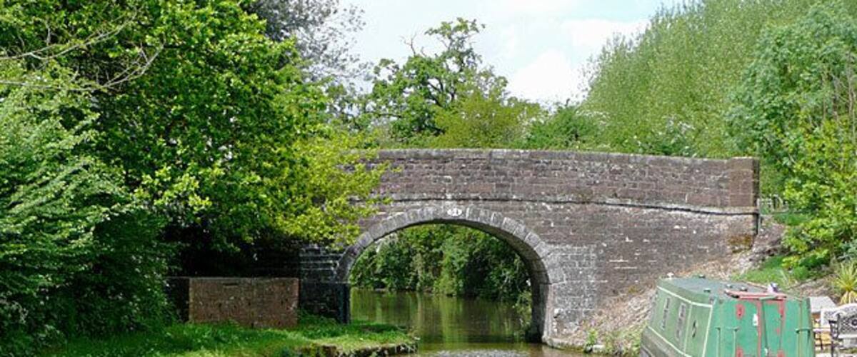 A stone bridge over a river, a green boat, and lush greenery.