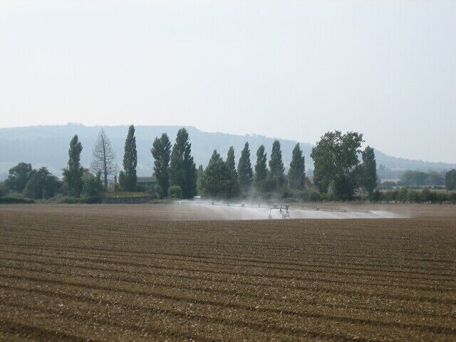Irrigation near Cropthorne. Looking south-west from the Pershore - Evesham road towards Bredon Hill. Most of the square is given over to farming with a small industrial works dealing in caterpillar tracks.