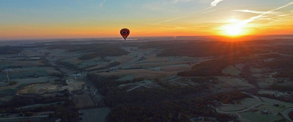 A hot air balloon over a rural landscape at sunset.